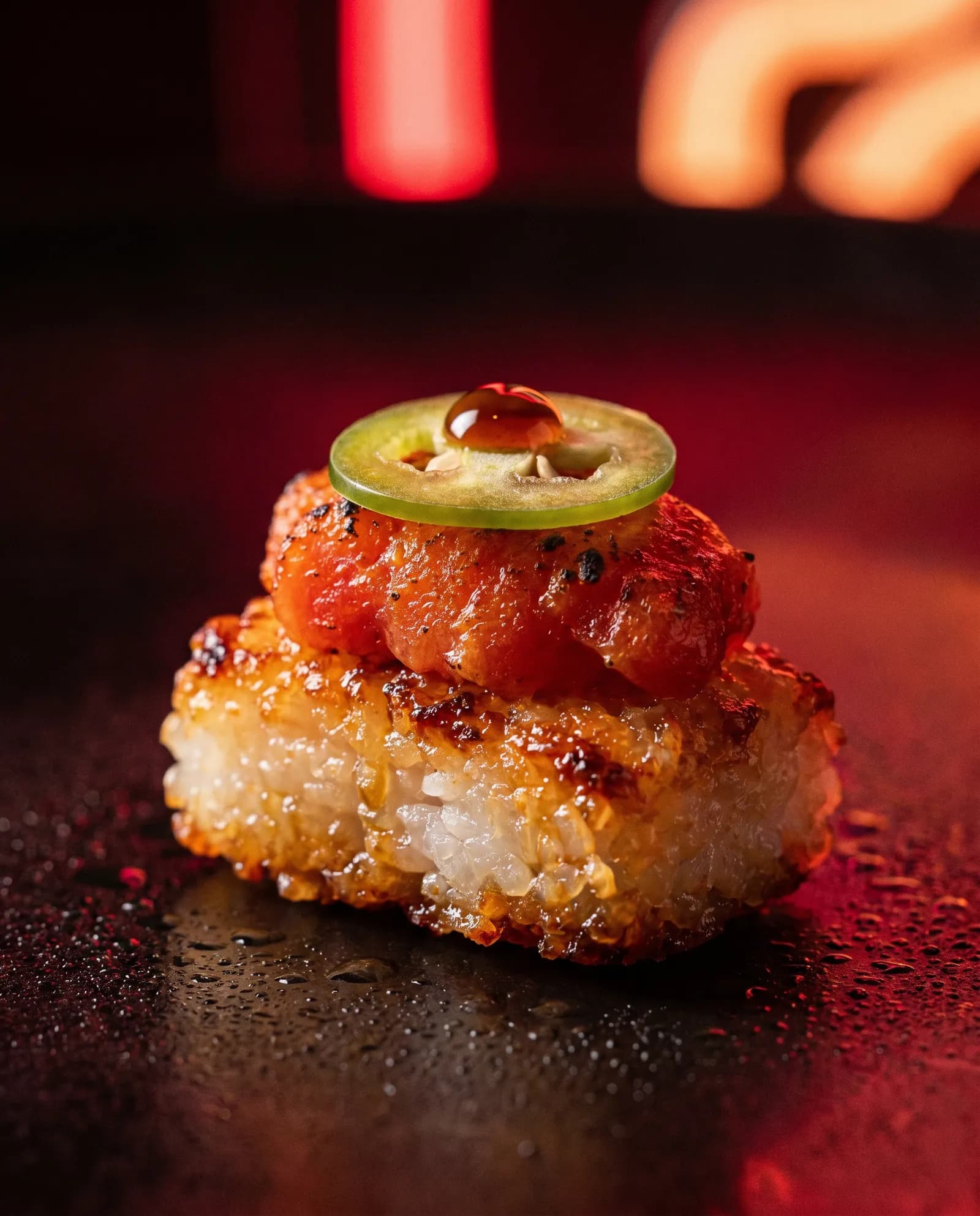 A torched crispy rice bite topped with spicy tuna and jalapeño