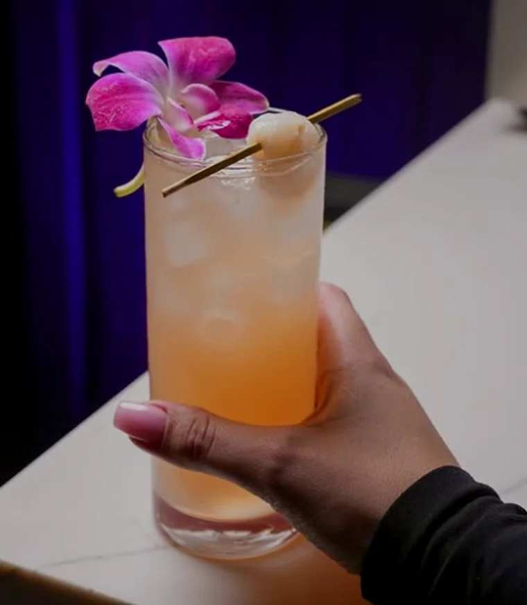 A lychee and orchid highball held above the marble counter
