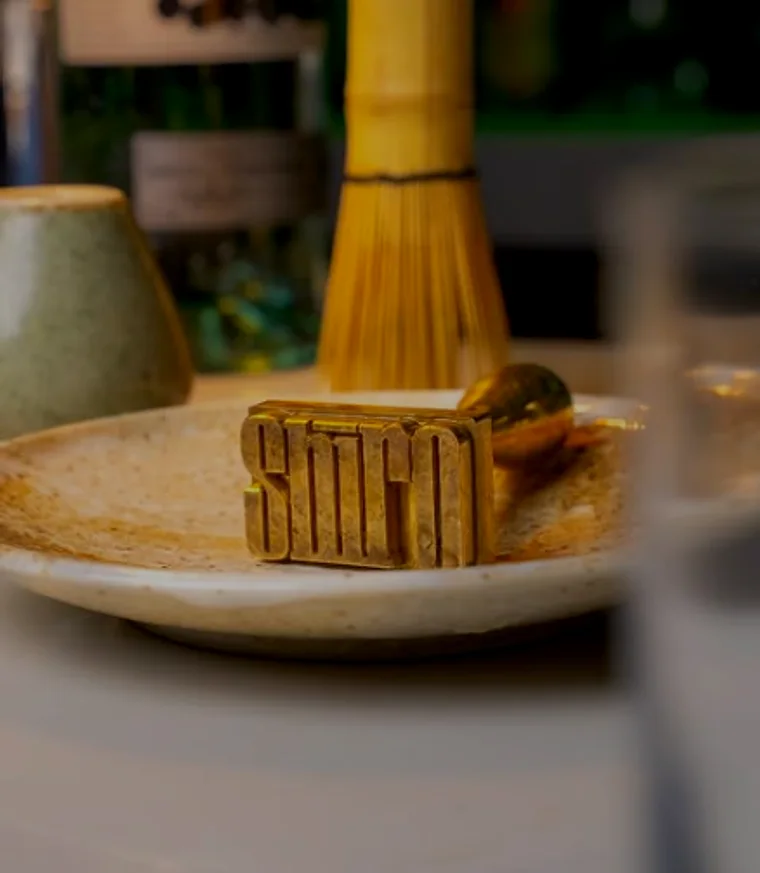 A bamboo matcha whisk and a SHIRO-branded block on a ceramic plate