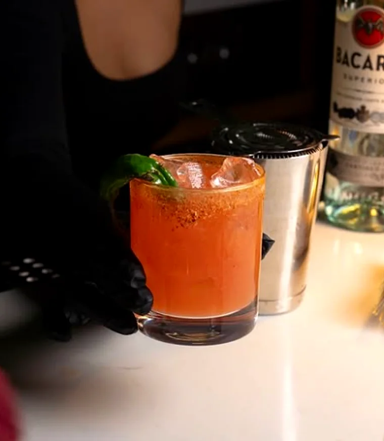A finished cocktail beside a shaker and bottles at the bar