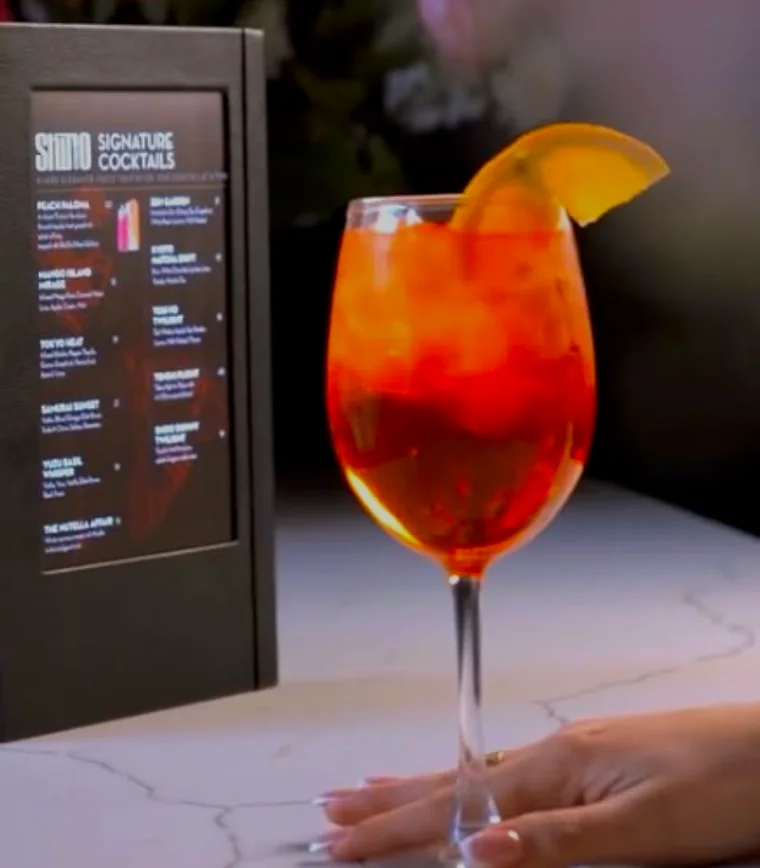 A spritz in a wine glass beside the SHIRO signature cocktails board
