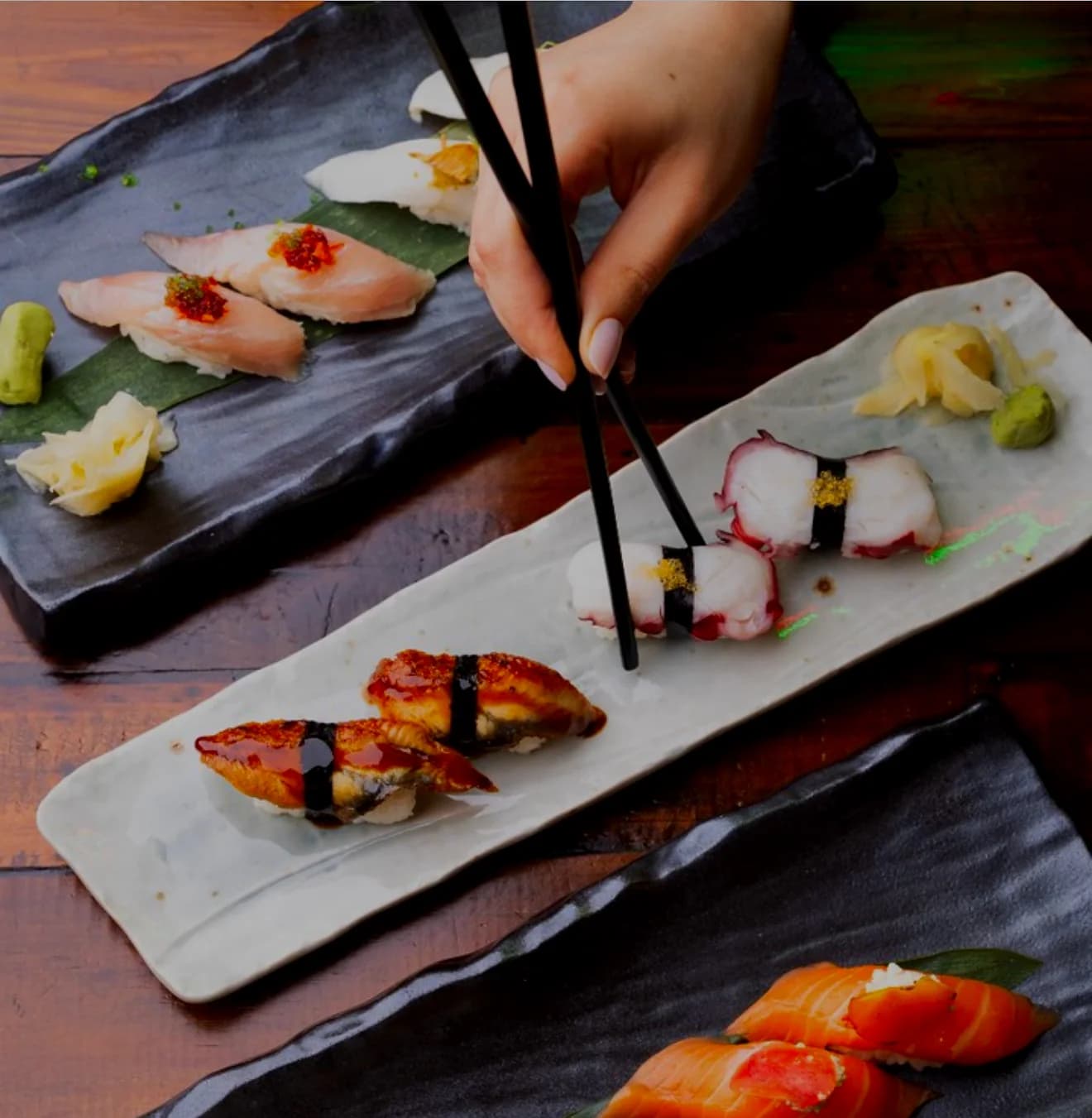 Nigiri flight on slate boards, chopsticks reaching in