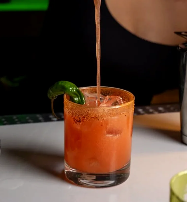 A cocktail being poured into a chilli-rimmed glass