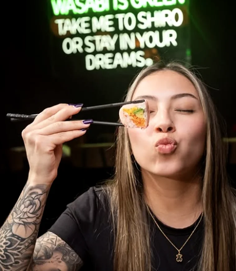 A guest holding a roll on chopsticks in front of the neon sign