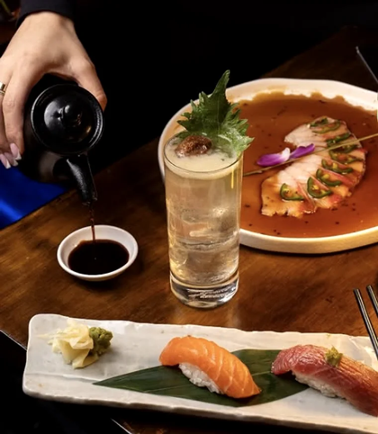 Soy sauce being poured beside a sashimi plate and a board of nigiri